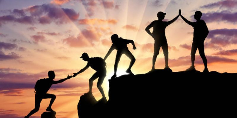 Silhouette of five climbers who climbed to the top of the mountain working in a team. Conceptual scene of alpinists and teamwork